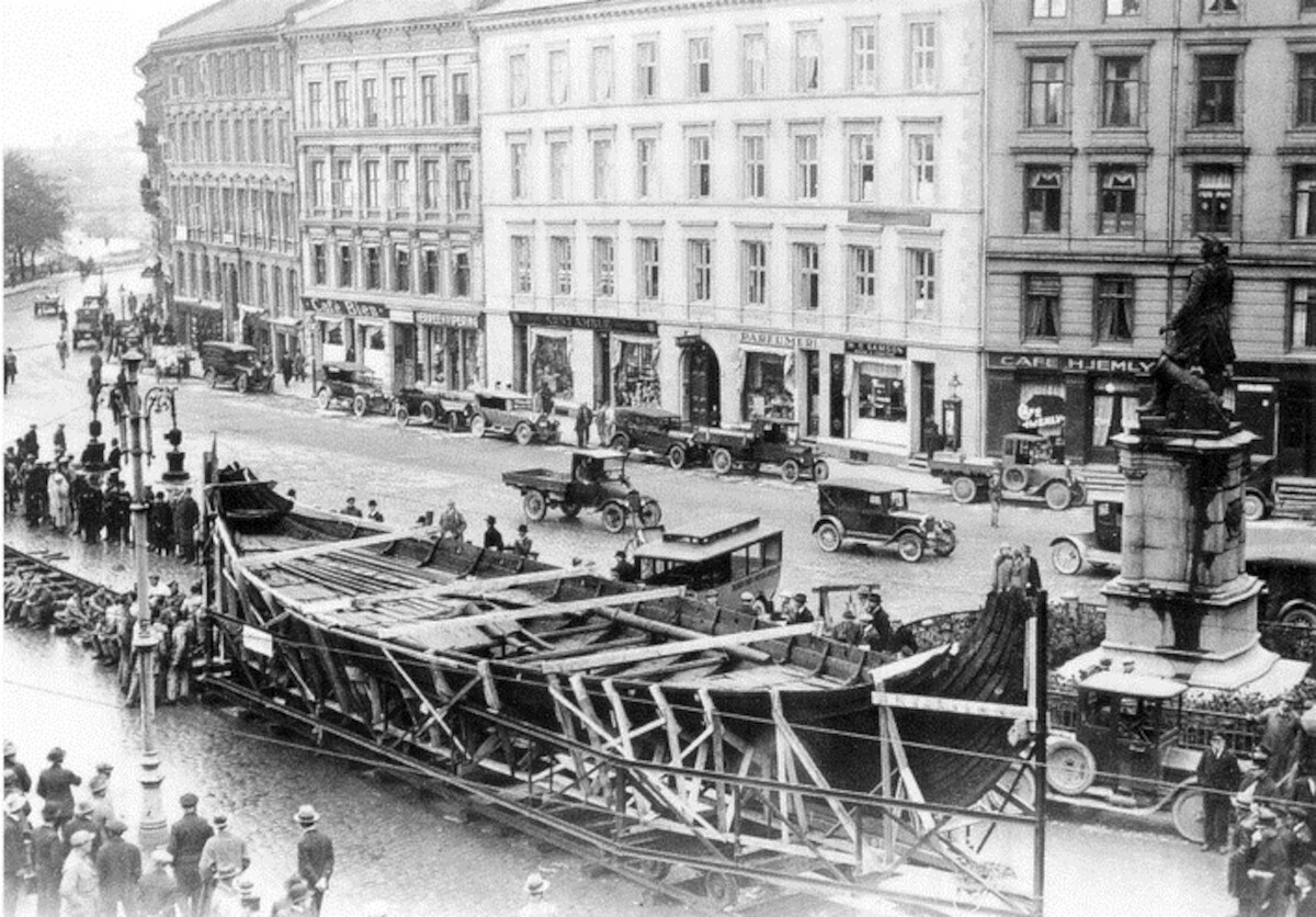 Transport łodzi z Osebergu do Muzeum Statków Wikińskich na półwyspie Bygdøy w Oslo w 1926 r. Źródło: <a href='https://en.wikipedia.org/wiki/Oseberg_Ship#/media/File:Flytting_av_Osebergskipet_p%C3%A5_skinner_langs_Sj%C3%B8gata_mot_Bygd%C3%B8y_A-70091_Ua_0003_282.jpg'>domena publiczna </a>.